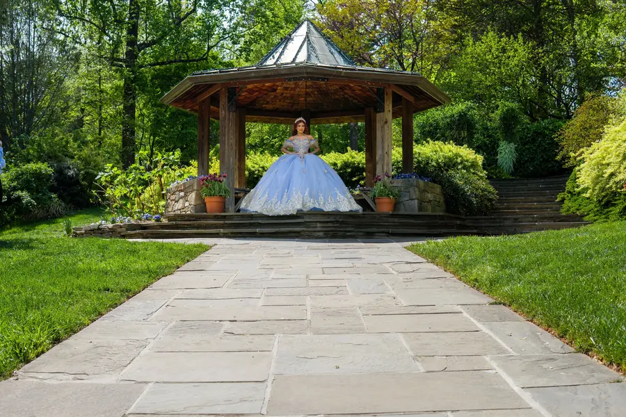Quinceañera in blue gown at a garden gazebo